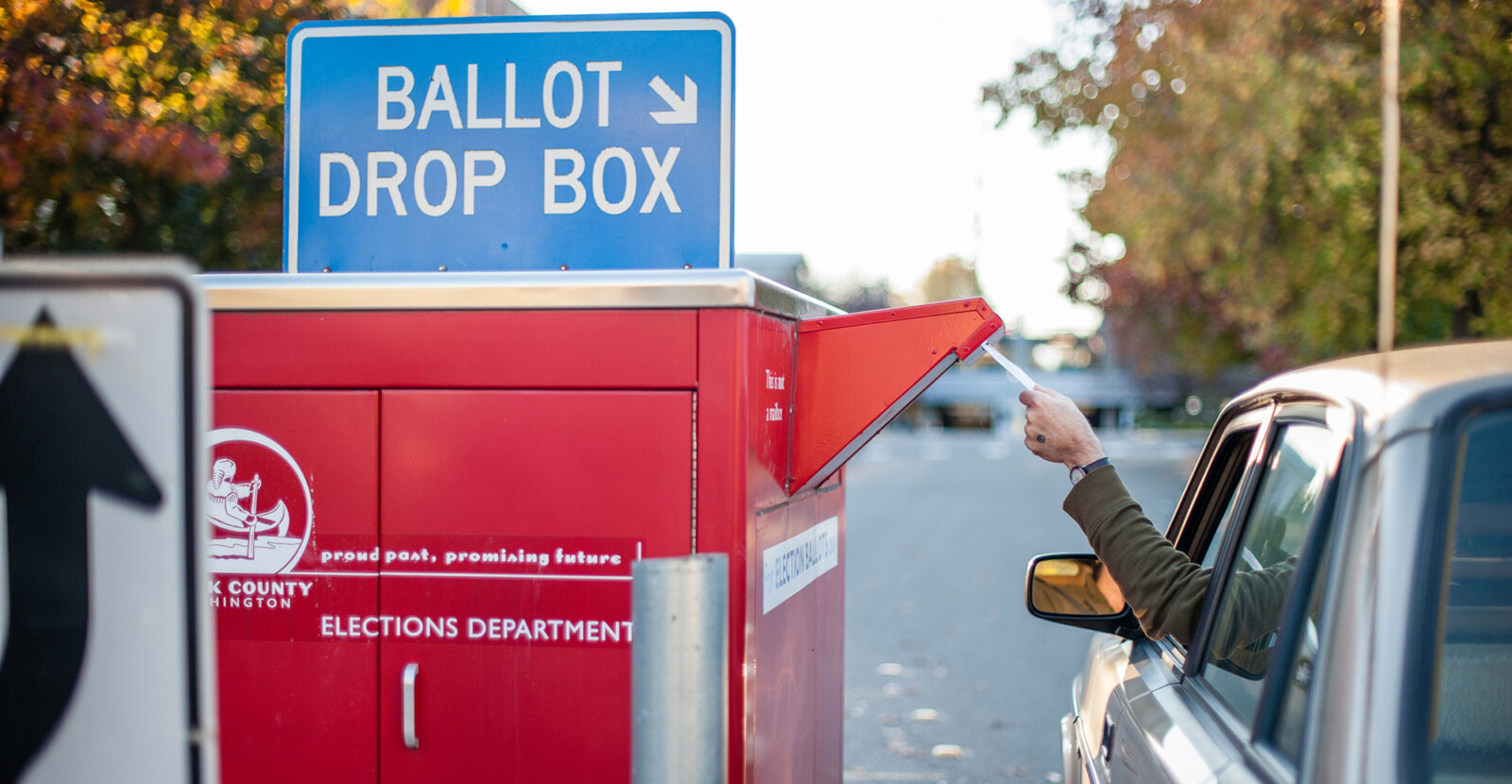 person in a car dropping their election ballot in a drop box